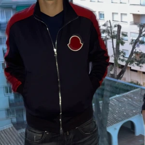 Moncler Cardigan Tjocktröja - Säljer en snygg blå jacka med röda detaljer och dragkedja framtill. Den har ett coolt märke på bröstet och är perfekt för höst och vår. Jackan har långa ärmar och en normal passform. Perfekt för dig som vill ha en stilren look! Passar. både S och M. Kvitto finns och ges med beställning