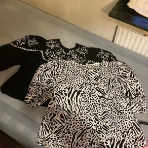 Svart blus med broderade blommor och vit mönstrad blus  - Två snygga blusar till salu! Den svarta blusen har vackra vita broderade blommor och puffiga armar perfekt för höst och sommar . Den vita blusen har ett djärvt svart mönster med både leopard- och zebrainspirerade detaljer, också med puffiga armar . Båda är i mycket bra skick och passar perfekt för både vardag och fest.Den svarta är st 32 och den vita är st S . Båda för 350 och en st för 200 + frakt ( 59kr)
