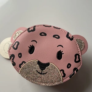 Rosa leopardmönstrad väska för barn - Supergullig rosa väska i form av ett djuransikte med leopardmönster. Den har en praktisk dragkedja och är perfekt för att hålla småsaker. Perfekt accessoar för en lekfull stil för barn.