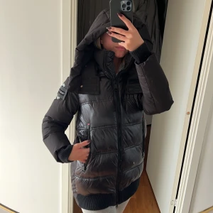 Svart dunjacka med huva - Säljer en svart varma vinterjacka som har en stor och bra luva. Glansigt material på framsidan, 2 fickor med dragkedja. Knappt använd i superfint skick. Storlek M med är mer som S skulle jag anse. (Spegel smutsig ej på jackan.) Säljer för 500 kr. Köparen står för frakten! 