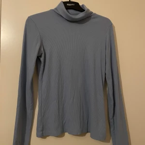 Ljusblå ribbad polotröja - Säljer en stilren ljusblå polotröja från NA-KD. Den är ribbad och har långa ärmar, perfekt för kyligare dagar. Tröjan är i mycket bra skick och passar både till vardags och lite finare tillfällen. Supermjuk och bekväm att ha på sig! 💙