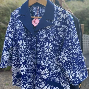 Blå blommig skjorta - Snygg blå skjorta med ett coolt blommigt mönster i vitt. Den har korta ärmar och en klassisk krage. Perfekt för sommarens alla fester eller bara en chill dag ute. Skjortan är i bra skick och redo för nya äventyr!