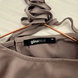 Beige topp från Gina Tricot - Säljer en snygg beige topp från Gina Tricot i storlek 36. Toppen har korta ärmar och en cool öppning i ryggen med en snöring runt midjan  som ger en unik look. Perfekt för både vardag och fest!