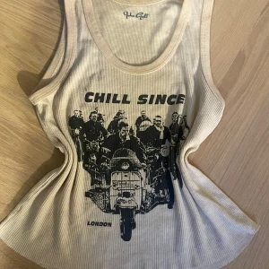 Beige ribbad linne med tryck - Säljer ett beige ribbat linne från Brandy Melville med ett coolt tryck av motorcyklister och texten 'Chill Since London'. Perfekt för en avslappnad stil. Linnet är i bra skick men har en liten fläck som syns på sista fotot💗💗