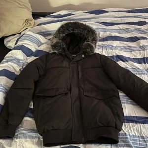 Mckenzie - Säljer en svart pufferjacka med mysig pälsdetalj på huvan. Perfekt för kalla vinterdagar. Jackan har långa ärmar och praktiska fickor framtill. Den är i mycket bra skick och håller dig varm och stilren hela säsongen.