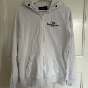 Vit hoodie från Peak Performance - Säljer en snygg vit hoodie från Peak Performance i bra skick. Saknar tyvärr snören. Storlek S. Personen på bilden är 180 cm lång.