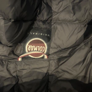 Svart pufferjacka från Colmar - Säljer en snygg svart pufferjacka från Colmar. Den är perfekt för kalla dagar med sitt quiltade mönster och långa ärmar. Jackan har en praktisk dragkedja och en mysig huva. Perfekt för både höst och vinter!