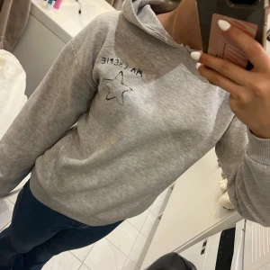 Grå hoodie från Gina Tricot - Säljer en mysig grå hoodie från Gina Tricot med texten 'MA CHÉRIE' och en stjärna på ryggen. Perfekt för en avslappnad stil. Snöret har krupit in i hoodien men det är lätt fixat om man är lite pillig, fortfarande i bra skick. Passar perfekt till jeans eller leggings!❤️