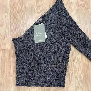 Snygg grå oneshoulder topp från H&M i återvunnen polyester. Perfekt för en stilren look med sin tighta passform och långa ärm. Toppen är croppad och passar utmärkt till både vardag och fest. Ett måste i garderoben för den modemedvetna! Helt oanvänd med prislappen på