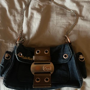 Blå axelväska med kedja - Säljer en snygg svart axelväska med kedja och coola detaljer. Köpt på Sellpy men har aldrig kommit till användning. Den är i bra skick men metallen är lite ofärgad som man ser på bilden. Kontakta mig vid frågor💕