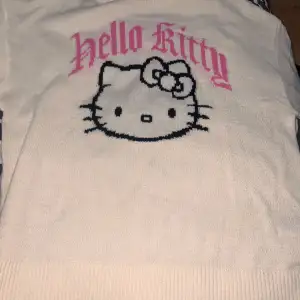 Superfin vit stickad tröja från H&M Divided med Hello Kitty-motiv i svart och rosa. Perfekt för alla Hello Kitty-fans! Tröjan har en normal passform och är i mycket bra skick. Den är både mysig och stilren, perfekt för höst och vinter.