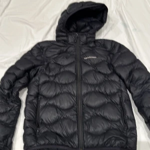 Svart dunjacka från Peak Performance - Säljer en svart dunjacka från Peak Performance i mycket bra skick. Jackan är perfekt för kalla dagar med sin quiltade design och huva. Den har en dragkedja framtill och är långärmad. Superbra för både höst och vinter!