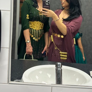 Vinröd klänning med gulddetaljer - Säljer en elegant vinröd klänning med gulddetaljer och bälte. Klänningen har en v-ringad design och är dekorerad med glittriga inslag. Perfekt för festliga tillfällen! Hyr gärna ut