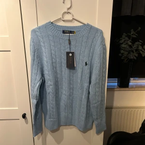 Ljusblå stickad tröja från Ralph Lauren - Säljer en superfin ljusblå stickad tröja från Ralph Lauren. Den är helt ny med taggar kvar och har ett klassiskt kabelstickat mönster. Perfekt för både höst och vår, med långa ärmar och en stilren design. Passar perfekt för en casual look eller lite mer uppklätt. 🧶💙