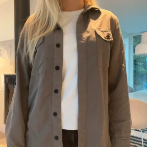 Brun overshirt med blommigt broderi - Denna kan användas som en overshirt eller kofta!❤️ Säljer en snygg brun/grön overshirt med blommigt broderi på ryggen från St. Tropez. Perfekt för höst och vår, och ger en cool touch till vilken outfit som helst. 