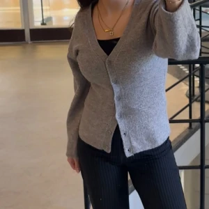 Grå kofta från Lindex - Säljer en figursydd beige kofta från Lindex i storlek XS. Den har en klassisk v-ringning och knappar framtill. Perfekt för både höst och vår, och funkar lika bra till vardags som till lite finare tillfällen. Koftan är i mycket bra skick och gjord av mjukt material som håller dig varm och bekväm.  