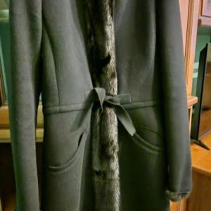 Svart kappa från Prada - Elegant svart kappa från Prada med pälsdetaljer på krage och ärmslut. Tillverkad i Italien med en blandning av ull och minkpäls. Kappan har en klassisk design med knytband i midjan för en figursydd passform.