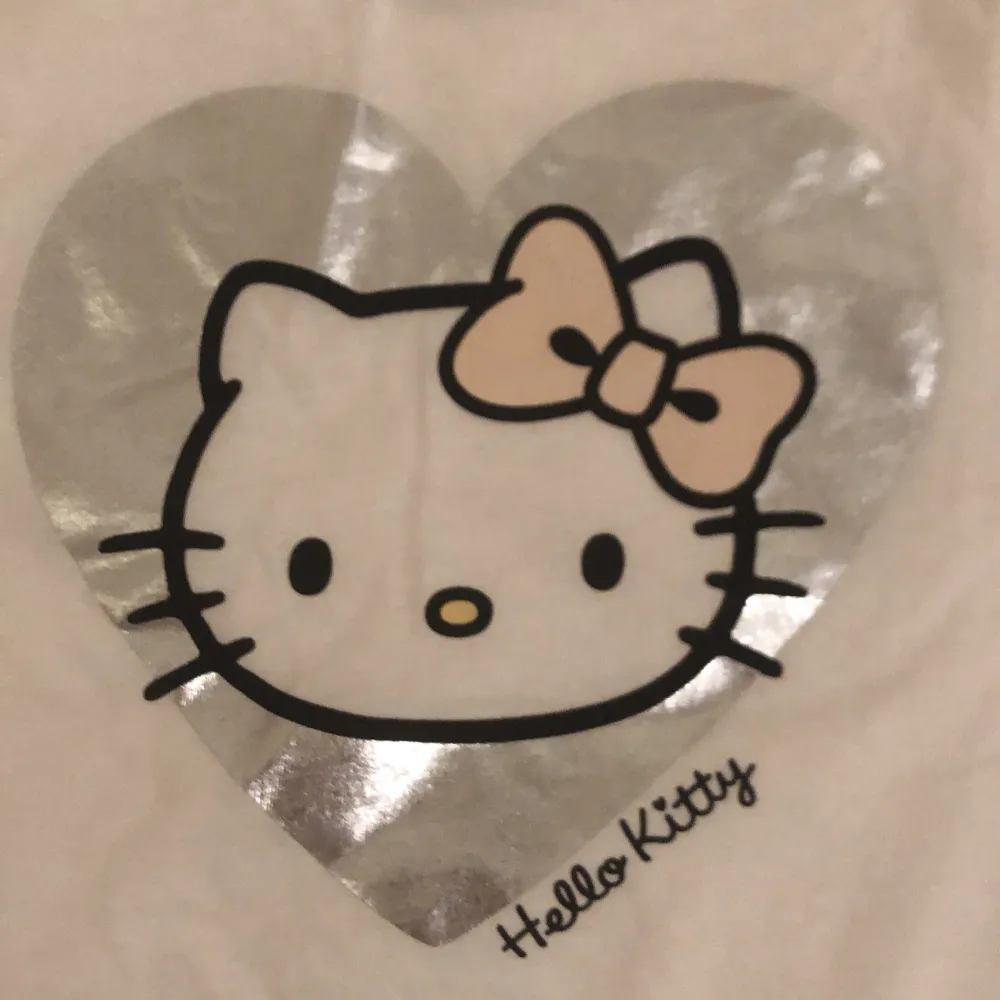 Söt vit t-shirt från H&M med ett stort Hello Kitty-tryck i silver och rosa. Perfekt för alla Hello Kitty-fans! T-shirten har korta ärmar och är gjord i mjukt bomullsmaterial.. T-paidat.