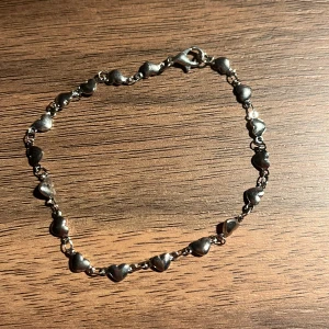 Silverfärgat armband med hjärtan - Charmigt armband i silverfärg med små hjärtan längs hela kedjan. Perfekt för att ge en romantisk touch till din stil. Armbandet har en praktisk karbinhake för enkel på- och avtagning.