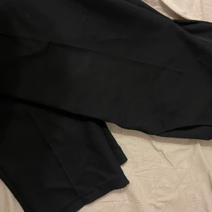 Svarta raka lösa byxor från NA-KD - Snygga svarta byxor från NA-KD i storlek 44. Perfekta för en stilren look. Byxorna har en klassisk design och är tillverkade i ett bekvämt material. Räfflat tyg. Benslutet behöver eventuellt sys upp.