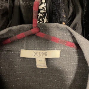 Grå randig skjorta från Dagmar - Snygg grå skjorta från Dagmar med diskreta ränder och klassisk krage. Skjortan har långa ärmar med knappar vid ärmsluten. Puffiga axlar, Perfekt för en stilren look.