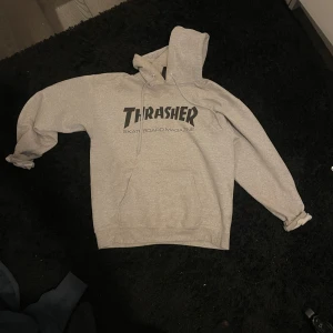 Grå hoodie från Thrasher - Säljer en grå hoodie från Thrasher med det klassiska logotrycket i svart på bröstet. Perfekt för skate eller chill dagar. Den har en stor huva och en bekväm passform.