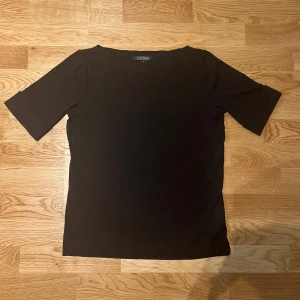 Svart topp från Lauren Ralph Lauren - Snygg svart topp från Lauren Ralph Lauren i bomull med trekvartsärm. Perfekt för en stilren look. Diskret RL-logga broderad vid fållen.