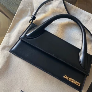 Svart Jacquemus väska  - Svart handväska från Jacquemus i skinn med ett stilrent och minimalistiskt design. Väskan har ett handtag och en axelrem för mångsidig användning. I nytt skick, pris kan diskuteras vid snabbt köp.
