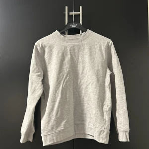 Grå sweatshirt från East West - Säljer en stilren grå sweatshirt från East West i storlek M. Tröjan har en klassisk design med rund hals och långa ärmar.
