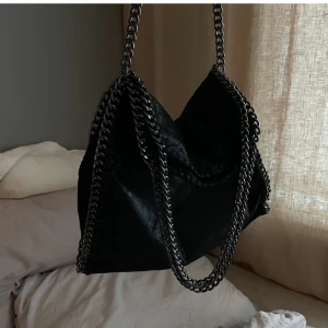 Svart axelväska med kedjedetaljer - Snygg svart axelväska med coola kedjedetaljer. Perfekt för att ge din outfit en edgy touch. Väskan har en stilren design och är lätt att matcha med olika stilar.