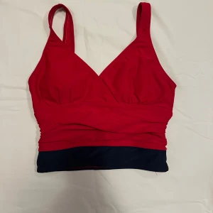 Röd och marinblå topp från Body I.D.  - Snygg röd topp med marinblå kant från Body I.D. Toppen har breda axelband och vadderade kupor för extra stöd. Perfekt för en sportig look eller en avslappnad dag.