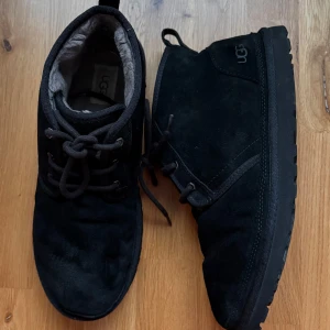 Svarta UGG Neumel kängor strlk 46 - Säljer ett par svarta kängor från UGG i mocka med snörning. De har en mjuk insida och en slitstark sula, perfekta för kyligare väder. Skorna är i storlek herr 46 och kommer i originalförpackning. Visst slitage syns på mockan men annars felfria. 