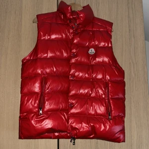 Röd moncler väst - Snygg röd dunväst från Moncler storlek 3 som motsvarar medium men skulle även passa större. Perfekt för kyligare dagar och ger en stilren look.