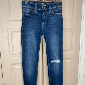 Blå jeans från O Denim - Snygga blå jeans från O Denim med en slitning på ena benet. De har en klassisk femficksdesign och en bekväm passform. Perfekta för en avslappnad stil.