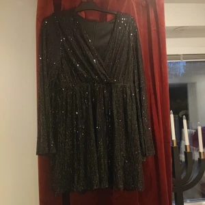 Svart glittrig klänning - Snygg svart klänning med glittriga detaljer och omlott-design. Den har långa ärmar och en v-ringad halslinje, perfekt för festliga tillfällen.