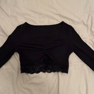 Svart croppad topp från Shein - Snygg svart croppad topp från Shein med spetsdetaljer och ribbad struktur. Toppen har långa ärmar och en knytdetalje framtill.