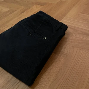 Dondup Manchesterbyxor mörkblå – Made in Italy - Material: 100% bomullsmanchester – mjukt, slitstarkt och stilrent 	•	Storlek: 31 – modern och bekväm passform 	•	Skick: Väldigt fint skick, knappt använda 	•	Färg: Mörkblå – elegant och mångsidig 	•	Design: Klassiskt italienskt hantverk 	Extra: Originalknapp medföljer som reserv  -Exklusiva mörkblå manchesterbyxor från Dondup, tillverkade i Italien. Dessa byxor kombinerar sofistikerad stil med hög komfort och passar perfekt för både vardag och mer uppklädda tillfällen. 