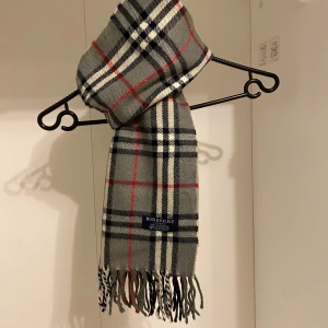 Burberry - Säljer nu denna Snygga halsduk från Burberry i färgen grå. Tillverkad i mjukt lammull med klassiskt fransad kant. Perfekt för att hålla dig varm och stilren under kyliga dagar. Hör av er vid funderingar☺️