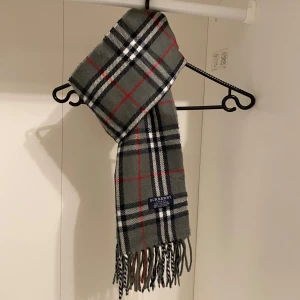 Burberry - Säljer nu denna Snygga halsduk från Burberry i färgen grå. Tillverkad i 100% mjuk kashmir med klassiskt fransad kant. Perfekt för att hålla dig varm och stilren under kyliga dagar. Hör av er vid funderingar☺️