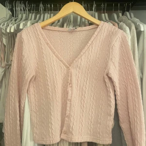 Rosa stickad kofta från Holly's - Säljer en söt rosa stickad kofta från Holly's i storlek S. Koftan har en v-ringad design med knappar framtill och ett fint kabelstickat mönster. Alla knappar finns men det är små hål vid armslutet. 🦌❄️ öppen för prisförslag!!