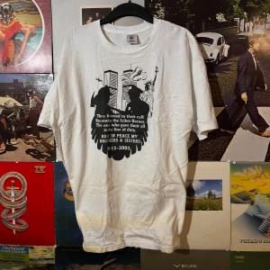 Vintage t-shirt med tryck från Delta - Vit t-shirt från Delta med ett stort svart tryck på framsidan som hedrar hjältar från 9-11-2001. Trycket visar silhuetter av brandmän och Frihetsgudinnan framför Twin Towers. Texten lyder: 'They listened to their call; Becoming the fallen Heroes. The ones who gave their all in the line of duty. REST IN PEACE MY BROTHERS & SISTERS 9-11-2001.'