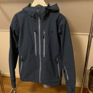 Skidjacka, Skogstad - Säljer en blå skaljacka från Skogstad med huva och RECCO-reflektor. Jackan är som ny och är endast använd två dagar i backen innan jag hann växa ur den.