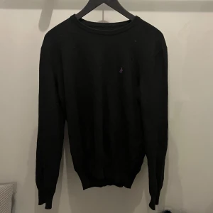 Svart stickad tröja från Ralph Lauren - Snygg svart tröja från Ralph Lauren med diskret logga på bröstet. Tröjan har en klassisk design med rund hals och långa ärmar. Perfekt för en stilren look. Framgår ingen storlek på tröjan men jag skulle säga M