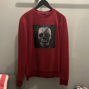 Röd sweatshirt från Limitato  - Snygg röd sweatshirt med ett stort dödskallemotiv på framsidan. Tröjan har en klassisk rund hals och långa ärmar. Perfekt för en cool och avslappnad stil. Kvitto finns och den är knappt använd.