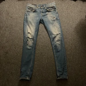 Dondup George - Snygga blå jeans från Dondup med slitna detaljer och en tight passform. Perfekta blåa färgen och trendiga slitningar. Den nyaste modellen George. Storlek 30
