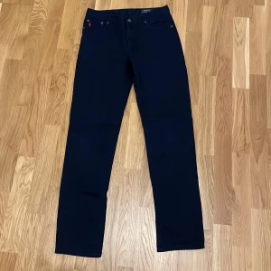 Polo Ralph Lauren Jeans - Snygga mörkblåa byxor från Polo Ralph Lauren med röd broderad logga på fickan. Byxorna har en klassisk design med knappar och är tillverkade i ett slitstarkt material.