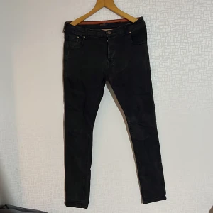 Svarta jeansbyxor från MG Star - Snygga svarta jeansbyxor från MG Star i normal passform. Byxorna har en klassisk design med knappar och dragkedja framtill. Perfekta för en stilren look.