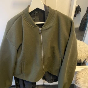 Olivgrön bomberjacka från Zara - Säljer en olivgrön bomberjacka från Zara med dragkedja framtill. Jackan har en klassisk bomberstil med ribbad krage och muddar. Perfekt för en stilren look.. Som en M i storleken 