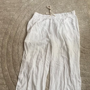 Vita linnebyxor med snörning - Säljer ett par vita linnebyxor med elastisk midja och snörning. Byxorna har en avslappnad passform och är perfekta för varma dagar. De har en enkel och stilren design med raka ben.