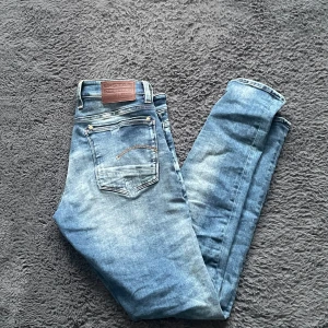 G-star jeans  - Snygga blå jeans från G-Star Raw med slitningar på knäna för en trendig look. De har en klassisk femficksdesign och en läderpatch med logga på baksidan. Perfekta för en avslappnad stil.